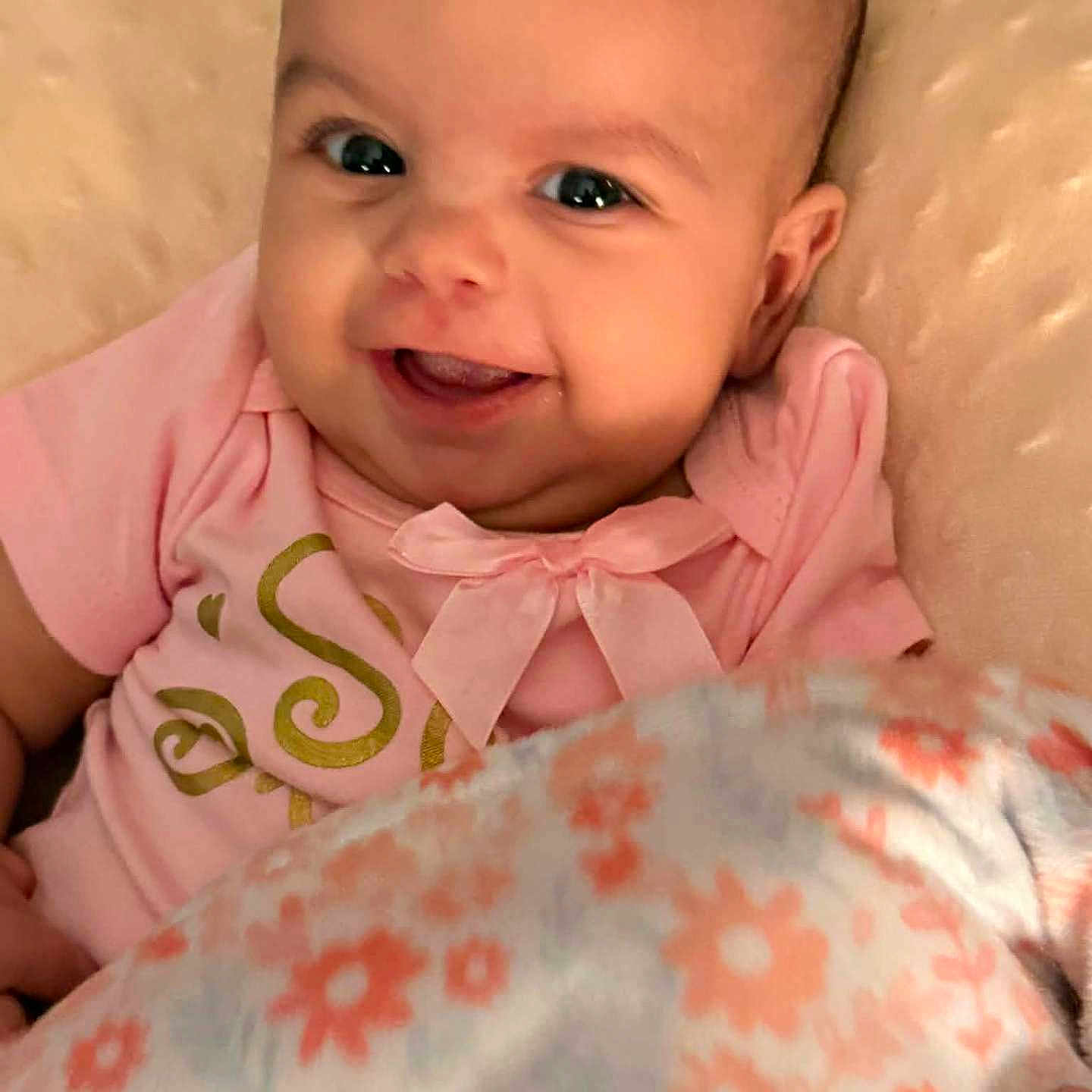 Jayda is registered to the contest to win money with this photo: baby, smiling, face, pink_clothing, blanket, floral_pattern, cute, infant, happy, portrait, child, cozy, indoors, head, skin, person, toddler, expression, warmth, comfort