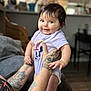 Melonie Me-Lon-e joined the competition — help win amazing prizes! baby, child, infant, smiling, tattoos, onesie, purple_clothing, indoor, person, cute, happy, face, hands, diaper, furniture, living_room, skin, short_hair, expression, holding