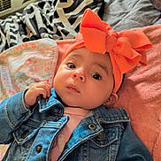 Aislynn is registered to the contest to win money with this photo: baby, denim_jacket, orange_bow, headband, blanket, indoor, infant, cute, face, portrait, child, clothing, soft_texture, lying_down, curious, young, person, cozy, patterned_blanket, casual
