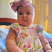 Madeline Galarza joined the competition — help win amazing prizes! baby, child, infant, headband, bow, floral_dress, arm, hand, bed, blanket, curtains, window, indoor, skin, face, eyes, cute, chubby, portrait, person