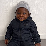 Mohamed participe au concours pour gagner de l'argent avec cette photo : child, toddler, smiling, sitting, black_tracksuit, nike_logo, beanie, gray_hat, happy, indoor, floor, wall, portrait, cute, young_child, fashion, casual_wear, person, clothing, headwear