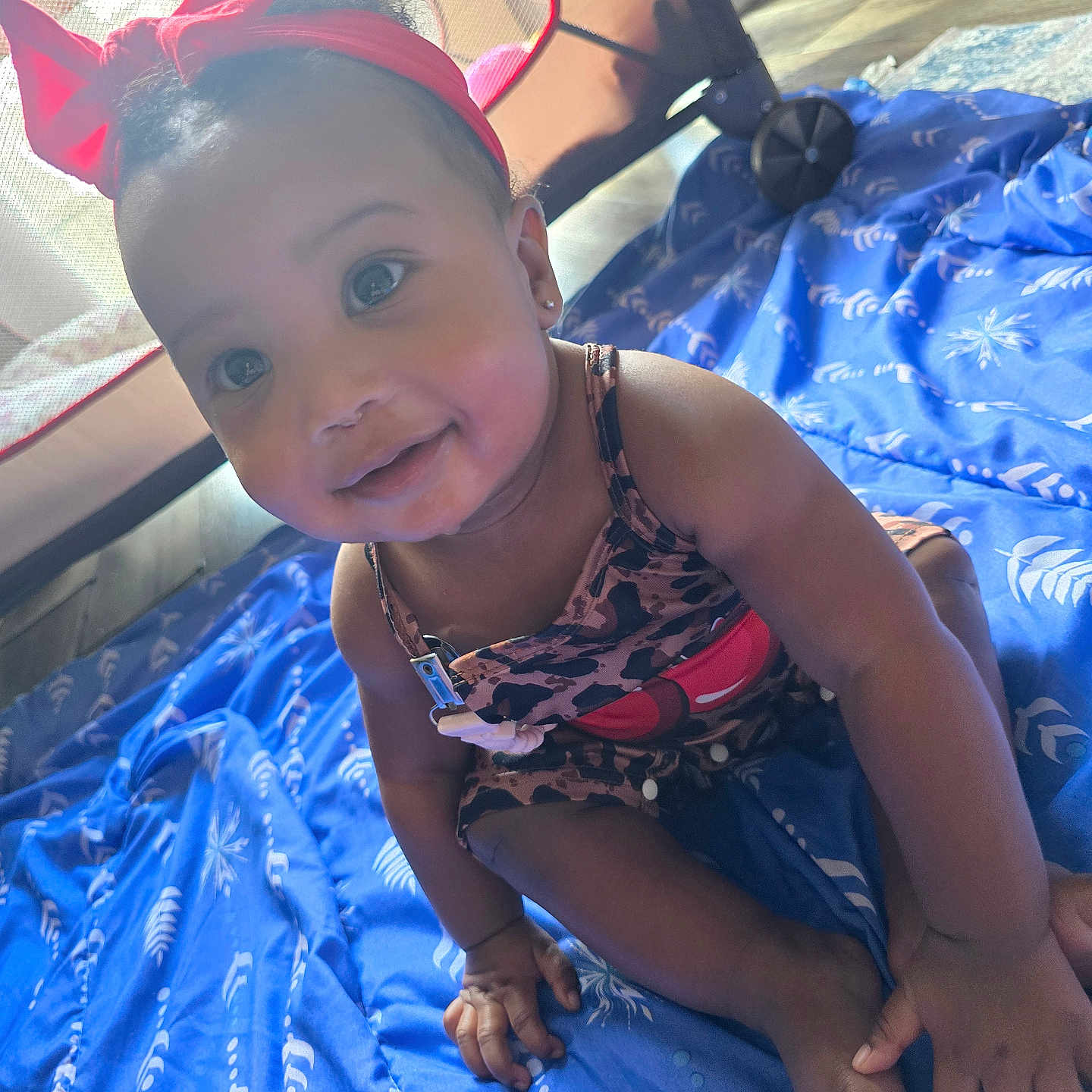 Honestee is registered to the contest to win money with this photo: baby, blue_blanket, child, clothing, cute, eyes, face, floor, foot, hand, happy, headband, indoors, infant, person, playpen, red_bow, sitting, skin, smiling