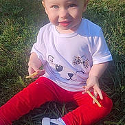 Lilly is registered to the contest to win money with this photo: toddler, child, grass, outdoor, white_tshirt, red_pants, sneakers, food, french_fries, happy, smiling, face, person, sitting, sunlight, cute, playful, hair, casual_clothing, nature