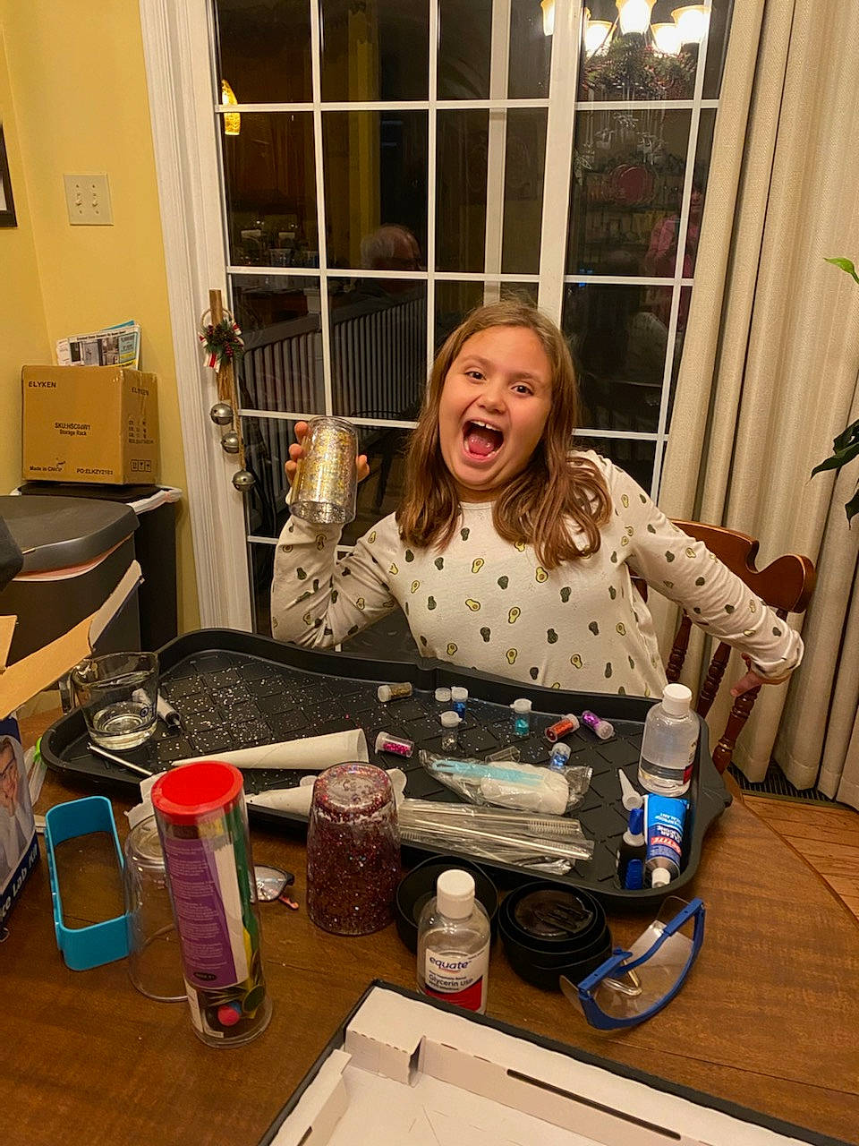 Kaelyn is registered to the contest to win money with this photo: bottle, box, cooking, countertop, curtain, drink, drinkware, fashion_design, flooring, fun, kitchen, liqueur, person, plastic_bottle, room, sitting, smile, t_shirt, table, water_bottle