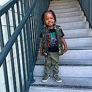 Kamari is registered to the contest to win money with this photo: child, stairs, smiling, camouflage, vest, tshirt, pants, shoes, outdoor, railing, concrete, person, fashion, happy, portrait, hair, braids, casual, footwear, daylight