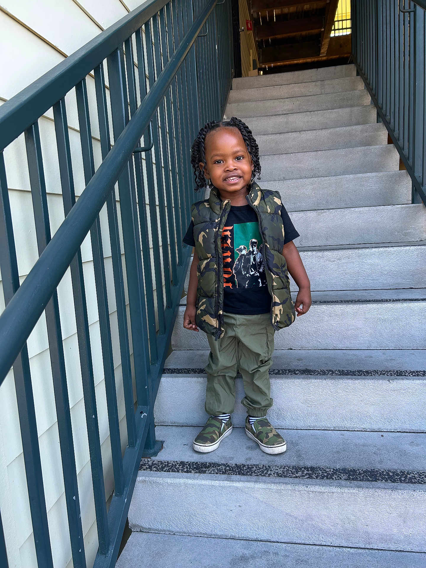Kamari is registered to the contest to win money with this photo: child, stairs, smiling, camouflage, vest, tshirt, pants, shoes, outdoor, railing, concrete, person, fashion, happy, portrait, hair, braids, casual, footwear, daylight