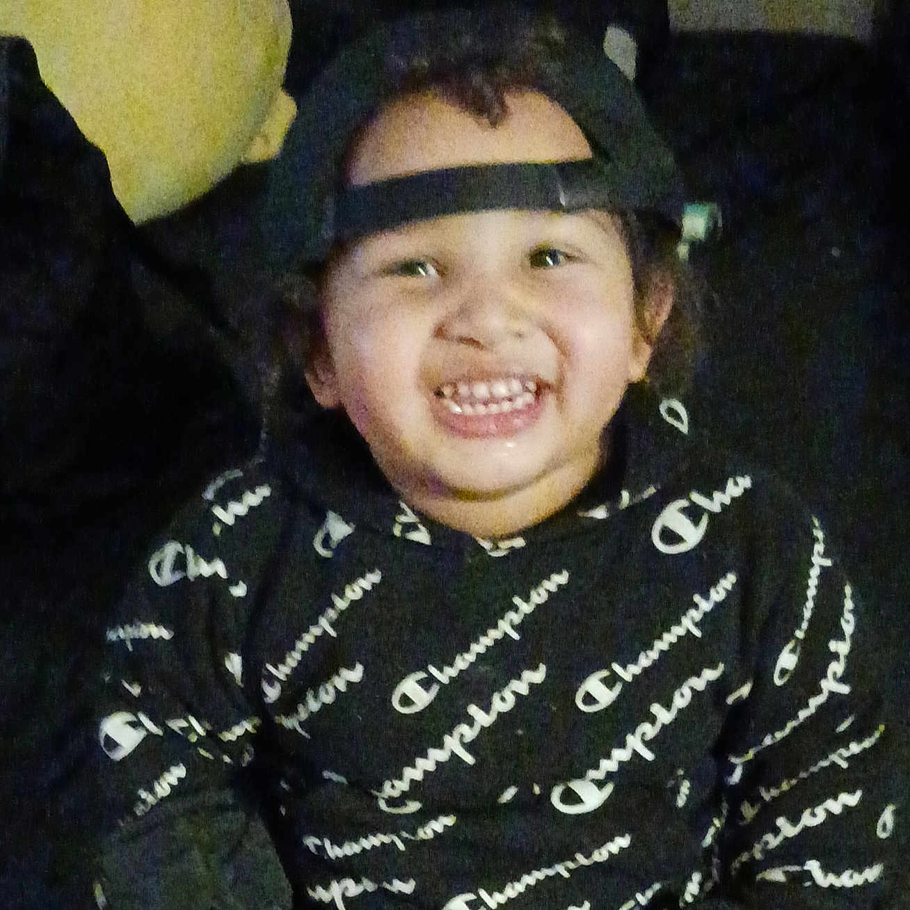 Jay'Quan is registered to the contest to win money with this photo: backwards_cap, black_hoodie, cap, casual_wear, cheerful, child, clothing, couch, cute, face, happy, hoodie, indoor, person, pillow, portrait, sitting, smiling, text_pattern, young