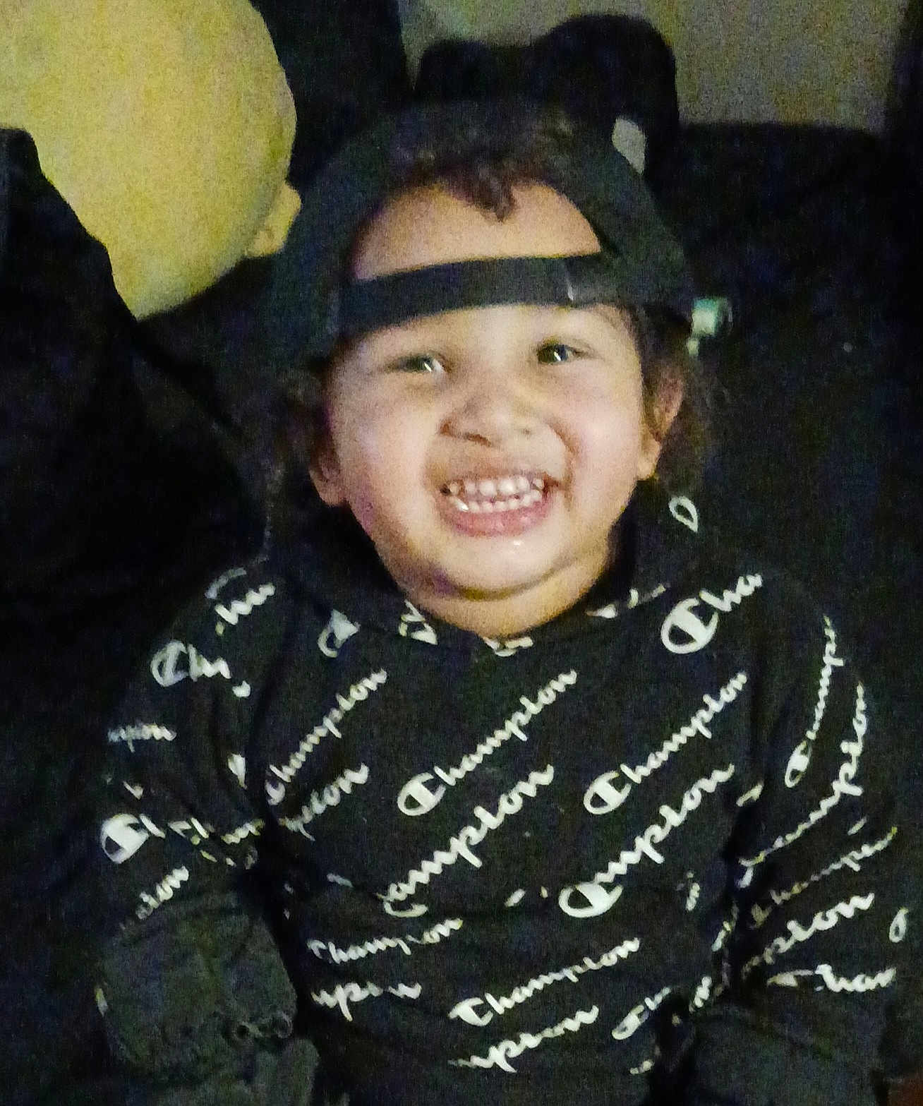 Jay'Quan is registered to the contest to win money with this photo: child, smiling, hoodie, cap, backwards_cap, sitting, indoor, couch, pillow, happy, person, face, clothing, casual_wear, young, portrait, cute, black_hoodie, text_pattern, cheerful