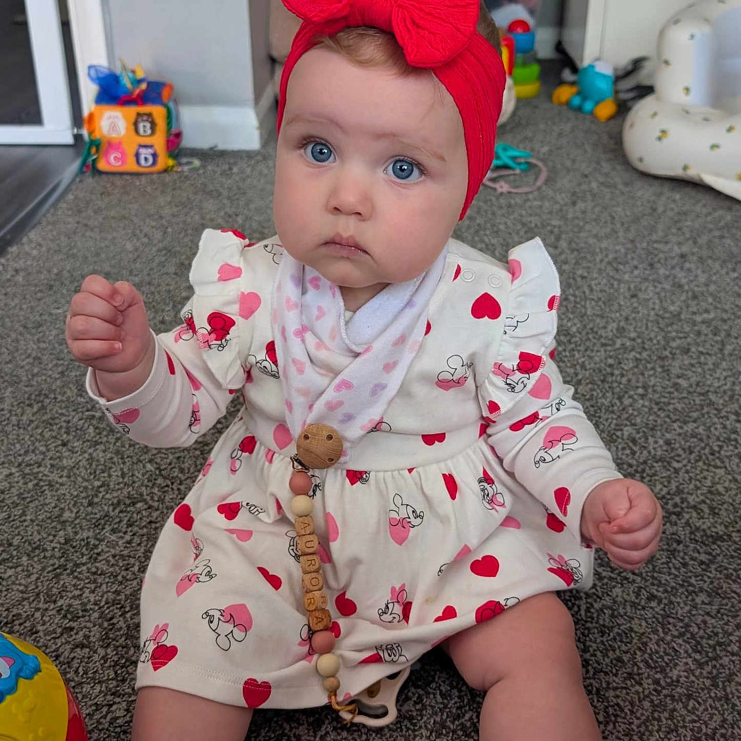 Aurora joined the competition — help win amazing prizes! baby, blue_eyes, carpet, child, colorful, curious, cute, dress, girl, headband, heart_pattern, indoor, infant, pacifier_clip, playroom, red_bow, sitting, sock, toy, wooden_beads