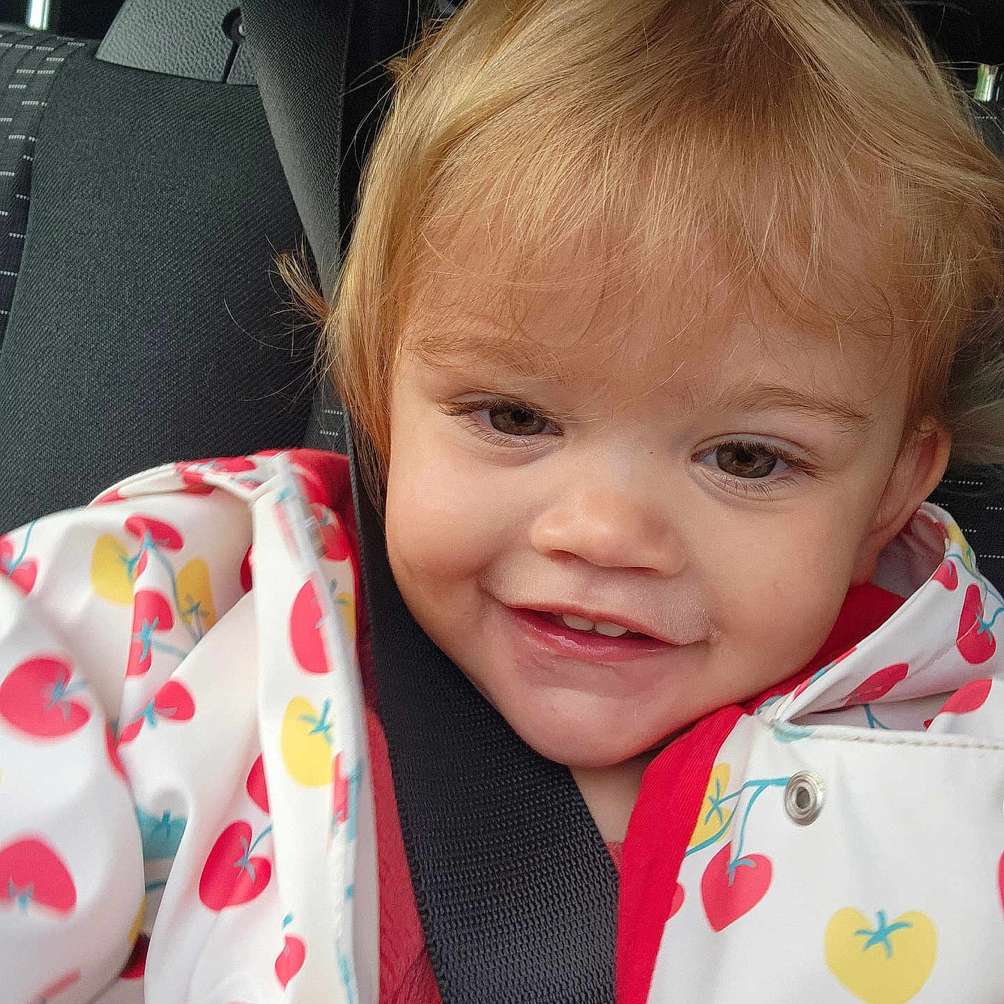 Méa participe au concours pour gagner de l'argent avec cette photo : car_interior, car_seat, casual, child, close_up, clothing, colorful, cute, expression, happy, indoor, light_brown_hair, person, portrait, raincoat, seatbelt, smiling, toddler, transportation, young_child