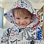toddler, child, hoodie, smile, face, indoor, person, clothing, cute, playful, expression, young, sleeve, fashion, casual, portrait, happy, headwear, room, blurry_background