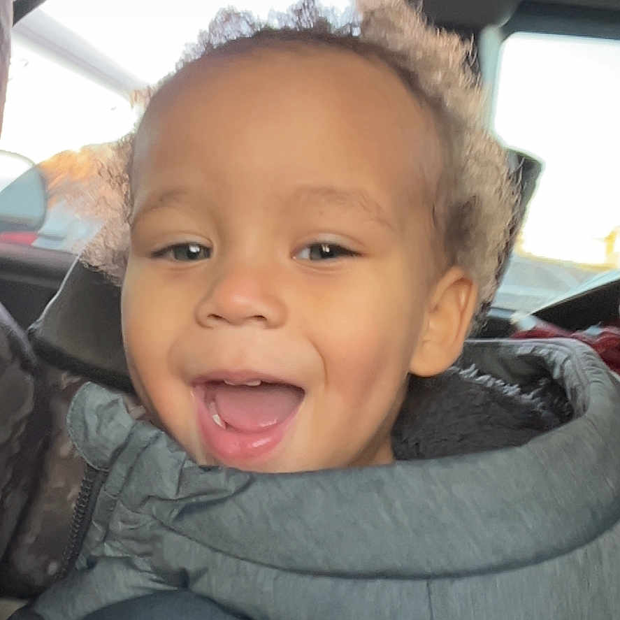 Carson is registered to the contest to win money with this photo: baby, bodypart, clothing, coat, cushion, face, finger, hand, happy, hat, head, homedecor, hood, jacket, mouth, person, photography, portrait, smile, teeth