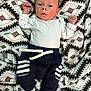 baby, infant, blanket, pattern, clothing, onesie, pants, socks, person, face, head, lying_down, newborn, cute, small, indoor, baby_garments, expression, hands_up, soft
