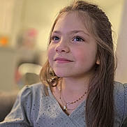 Sophie is registered to the contest to win money with this photo: child, girl, portrait, smile, long_hair, necklace, blouse, indoor, soft_light, closeup, face, young, thoughtful, casual_clothing, candid, happy, person, sitting, home, warm_tones