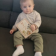 Charly participe au concours pour gagner de l'argent avec cette photo : baby, infant, child, sofa, couch, sweater, socks, pants, milestone_card, 7_months, holding, sitting, blue_eyes, portrait, home, cute, cardboard, illustration, smile, cozy