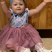 Mia is registered to the contest to win money with this photo: arms_raised, baby, boots, bow, carpet, child, costume, cowboy_boots, dress, fashion, happy, headband, indoor, infant, pink_skirt, portrait, sitting, smiling, sparkles, wooden_background