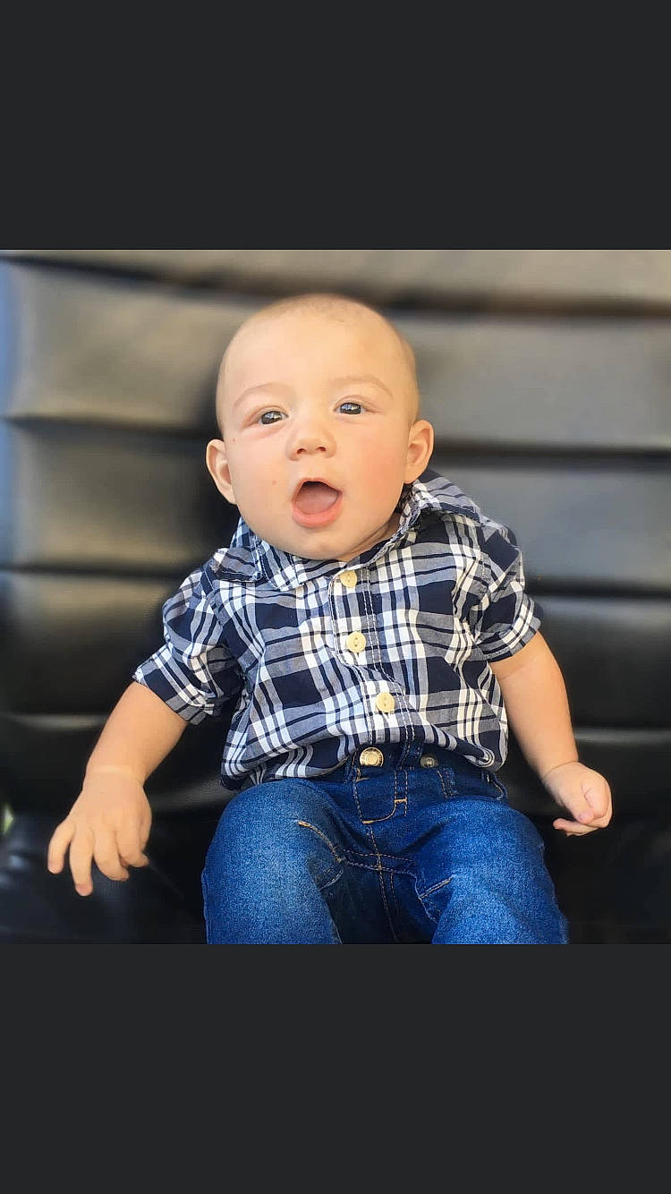 Johnathon is registered to the contest to win money with this photo: arm, baby, baby_toddler_clothing, cheek, child, collar, denim, dress_shirt, electric_blue, eye, flash_photography, happy, jeans, pattern, person, plaid, sitting, sleeve, surprise, t_shirt