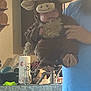 baby, costume, bull, kitchen, counter, paper_towel, soap_dispenser, person, hand, clothing, fuzzy, cute, indoor, holding, sink, appliance, blue_shirt, face, toy, animal_costume