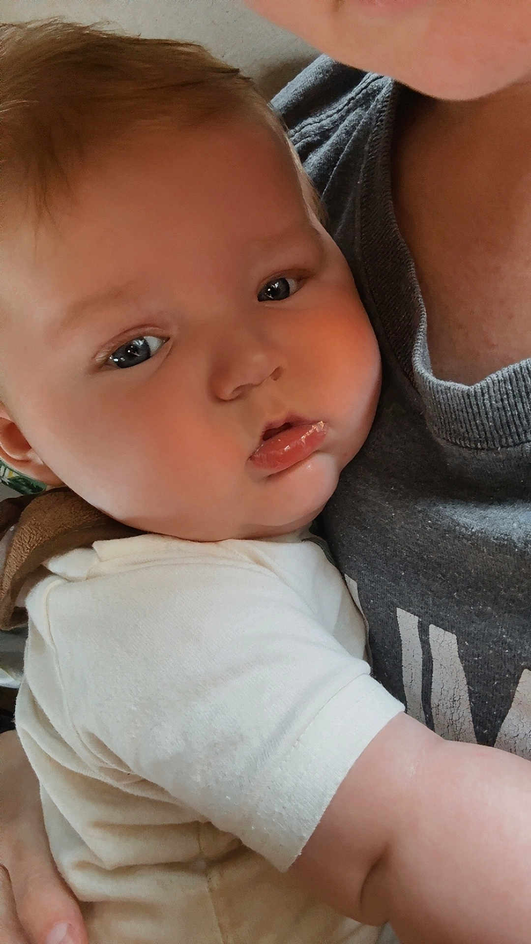 Hudson is registered to the contest to win money with this photo: baby, child, infant, face, skin, eyes, cheeks, arm, clothing, white_shirt, adult, holding, closeup, portrait, indoor, person, human, cuddling, gentle, soft_light