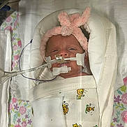 Zenalla is registered to the contest to win money with this photo: newborn, baby, hospital, medical_tubes, blanket, headband, pink, bunny_ears, lying_down, floral_pattern, face, swaddled, infant, healthcare, bed, cute, sleeping, white_blanket, person, child