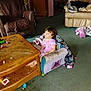Bella is registered to the contest to win money with this photo: child, toddler, pink_dress, small_chair, blanket, wooden_table, toys, carpet, living_room, sofa, armchair, curly_hair, indoor, furniture, relaxed, casual, messy, footwear_absent, person, home