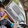Bella is registered to the contest to win money with this photo: child, car_interior, snack, chips, steering_wheel, socks, sneakers, window, vehicle, curly_hair, casual, seat, relaxed, candid, person, purple_shirt, gray_pants, greenery, truck, daylight