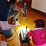 Bella joined the competition — help win amazing prizes! adult, tattoos, long_hair, flashlight, child, toddler, pink_jacket, pants, wooden_floor, device, cables, indoor, curious, exploration, barefoot, glasses, household, interaction, light, kneeling