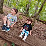 Bella is registered to the contest to win money with this photo: children, forest, tree_trunk, outdoor, nature, smiling, playful, boy, casual_clothing, greenery, leaves, wood, log, happy, sitting, young, daylight, pants, sneakers, trees