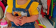 Bella is registered to the contest to win money with this photo: toddler, child, yellow_shirt, denim_overalls, indoor, clothing, washing_machine, sippy_cup, blanket, curly_hair, holding_object, colorful_clothes, laundry_room, cute, portrait, seated, baby, casual, home, expression