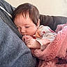 baby, sleeping, blanket, pink_blanket, person, hoodie, gray_hoodie, indoor, couch, cozy, child, infant, face, hand, soft_texture, comfort, rest, cute, peaceful, closeup