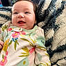 baby, child, smiling, face, blanket, striped_blanket, onesie, floral_pattern, indoor, cozy, happy, cute, infant, person, young_child, soft_texture, closeup, portrait, comfort, colorful_clothing
