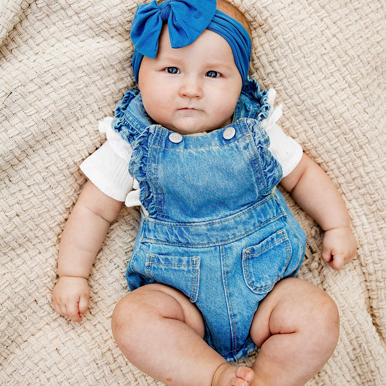 Lakelyn is registered to the contest to win money with this photo: baby, infant, child, portrait, lying_down, blanket, woven_texture, blue_headband, bow, denim_overalls, white_shirt, fashion, indoors, closeup, face, eyes, serious_expression, sitting_pose, cozy, photography
