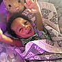 Zhyeed is registered to the contest to win money with this photo: baby, child, smiling, happy, blanket, plush_toy, rabbit, bed, cushion, pattern, purple_light, person, infant, raised_hands, cute, sleeping_area, comfort, indoor, soft_toy, portrait