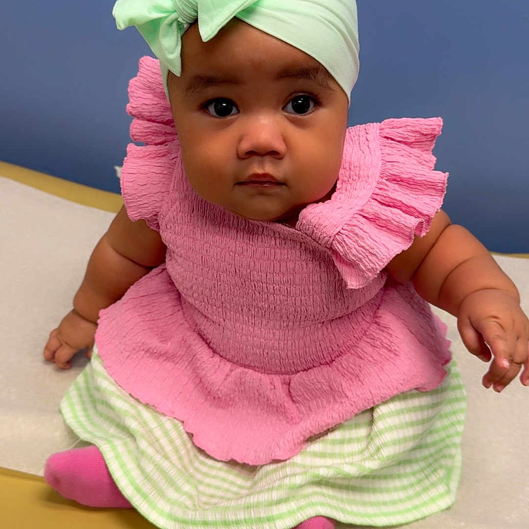 Siale joined the competition — help win amazing prizes! baby, child, headband, bow, pink_clothing, green_clothing, sitting, portrait, indoors, yellow_surface, blue_background, cute, serious_expression, infant, fashion, toddler, person, closeup, smiling, adorable