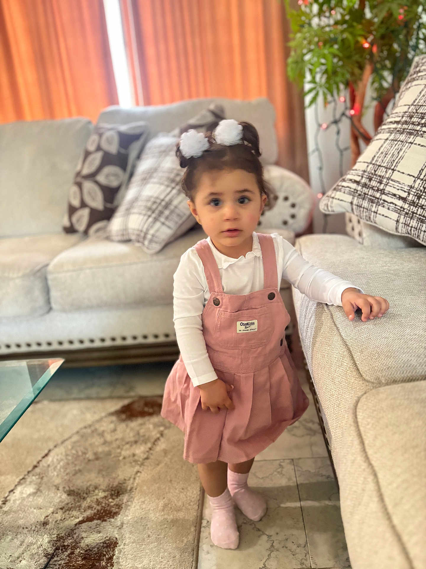 Amaly joined the competition — help win amazing prizes! child, toddler, girl, pink_dress, white_shirt, socks, living_room, couch, pillows, carpet, plant, hair_ties, floor, curious, indoors, furniture, home, portrait, standing, casual