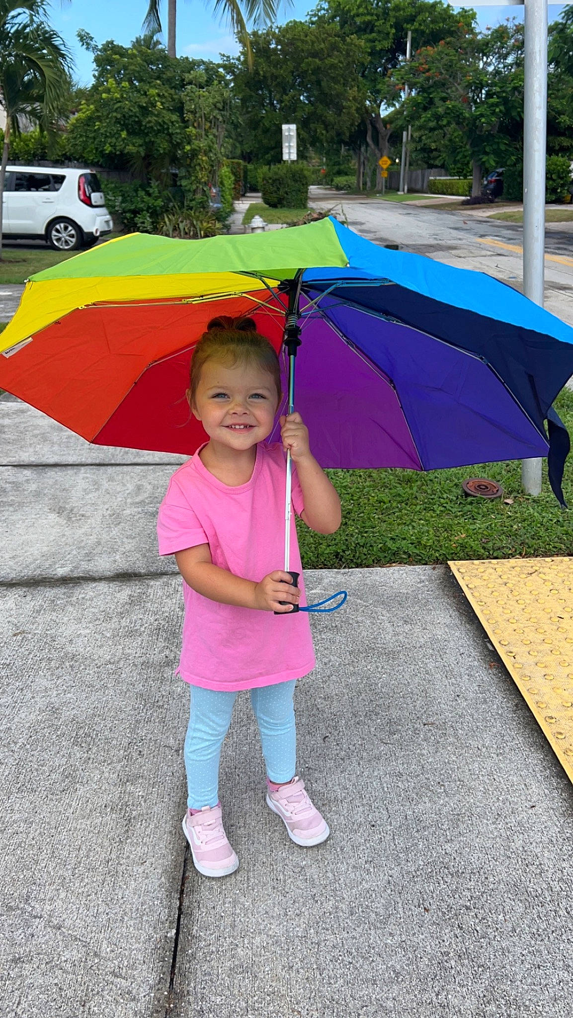 Cora is registered to the contest to win money with this photo: asphalt, child, fashion_accessory, fun, grass, joy, leisure, magenta, person, pink, plant, play, recreation, shade, smile, tints_and_shades, tire, toddler, tree, umbrella