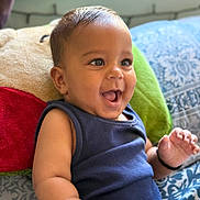 Jaiv is registered to the contest to win money with this photo: baby, smiling, child, infant, blue_clothing, pillow, indoor, happy, cute, face, portrait, sitting, skin, hand, expression, young_child, background, pattern, cozy, bright