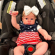 Gracelynn is registered to the contest to win money with this photo: baby, infant, car_seat, bow, dress, stars, stripes, raising_fist, child, indoor, seatbelt, cute, pink_skin, expression, headband, white_bow, person, young_child, clothing, sitting
