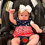 baby, infant, car_seat, bow, dress, stars, stripes, raising_fist, child, indoor, seatbelt, cute, pink_skin, expression, headband, white_bow, person, young_child, clothing, sitting
