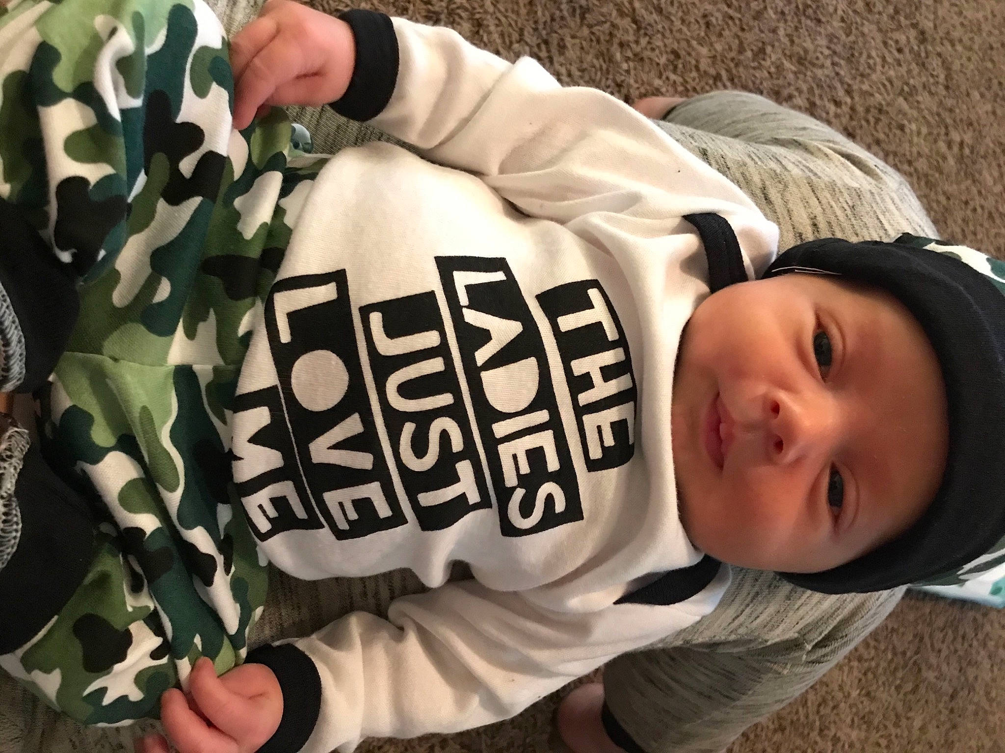 Haiden is registered to the contest to win money with this photo: baby, baby_toddler_clothing, camouflage, comfort, cool, finger, font, grass, hand, happy, headwear, military_camouflage, military_uniform, mouth, outerwear, person, sitting, sleeve, toddler, tree