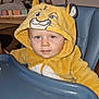 baby, child, high_chair, yellow_hoodie, lion_costume, face, blue_eyes, indoor, table, pumpkin, toy, furniture, person, hood, cute, expression, zipper, seat, room, soft