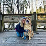 Boomer is registered to the contest to win money with this photo: woman, dog, wooden_dock, forest, trees, pond, leash, outdoor, nature, pet, canine, happy, tongue_out, casual_clothing, long_hair, sunlight, reflection, fence, kneeling, companion