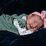 Olive is registered to the contest to win money with this photo: baby, newborn, smiling, sleeping, pink_bow, headband, green_dress, floral_pattern, soft_blanket, dark_background, peaceful, cute, infant, child, portrait, indoors, closeup, resting, happy, toddler