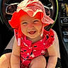 Olive is registered to the contest to win money with this photo: baby, child, smiling, hat, red_clothing, floral_pattern, car_interior, steering_wheel, dashboard, person, sitting, sunlight, happy, cute, infant, portrait, closeup, seat, lap, bright_colors