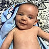 baby, infant, child, portrait, smiling, face, eyes, lying_down, blanket, blue_blanket, bed, bedding, patterned_background, indoors, close_up, bare_chest, happy, cute, photograph, head
