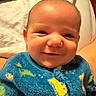 Kashtyn is registered to the contest to win money with this photo: baby, infant, child, smiling, portrait, close_up, blue_outfit, dinosaur_pattern, fuzzy_clothing, bed, blanket, bedding, indoor, cozy, happy, face, head, eyes, nose, photography