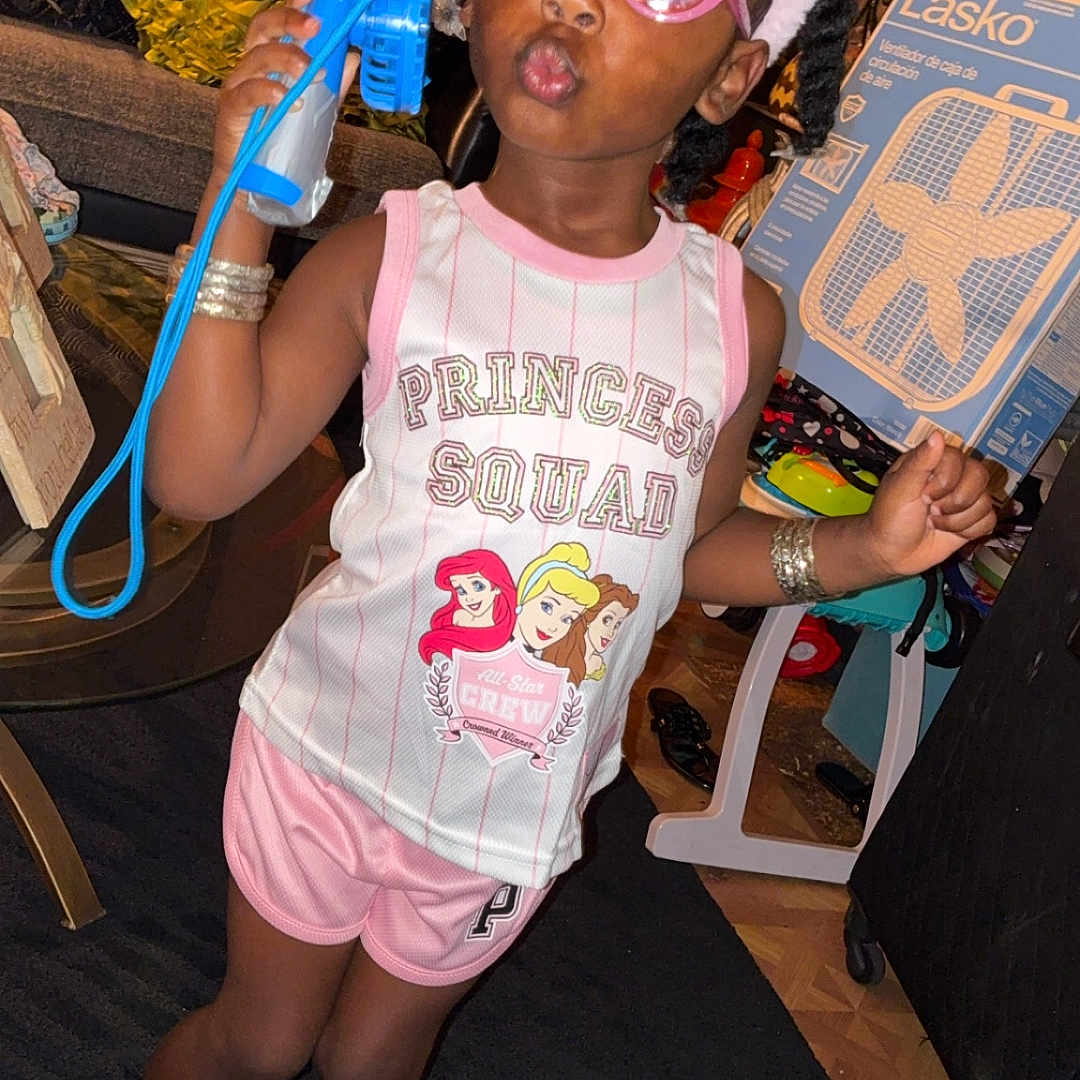 Aartaviah is registered to the contest to win money with this photo: child, girl, toddler, portrait, indoors, smiling, pouting, sunglasses, pink_hat, cat_ears, princess, dress, shorts, bracelets, toy_fan, toy, fashion, sitting, living_room, playful