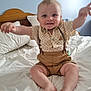 arms_raised, baby, bed, blue_wall, child, cute, feet, furniture, happy, head, indoor, person, polka_dot_shirt, portrait, shorts, sitting, smiling, suspenders, toothy_grin, white_bedding