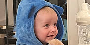 Emrys is registered to the contest to win money with this photo: baby, baby_bottle, baby_clothing, blue_hoodie, child, cozy, cushion, cute, fluffy_toy, happy, home, indoor, infant, person, playful, portrait, seated, smiling, soft_toy, young_child