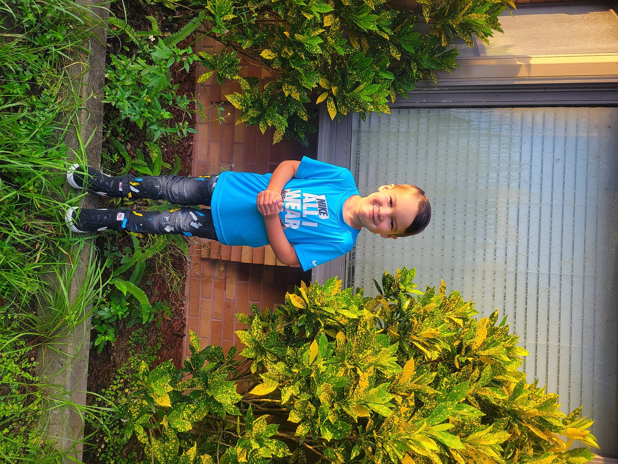 Keenan is registered to the contest to win money with this photo: botany, electric_blue, grass, groundcover, happy, hat, joy, leaf, leisure, people_in_nature, person, plant, shrub, smile, snapshot, spring, t_shirt, toddler, tree, vegetation